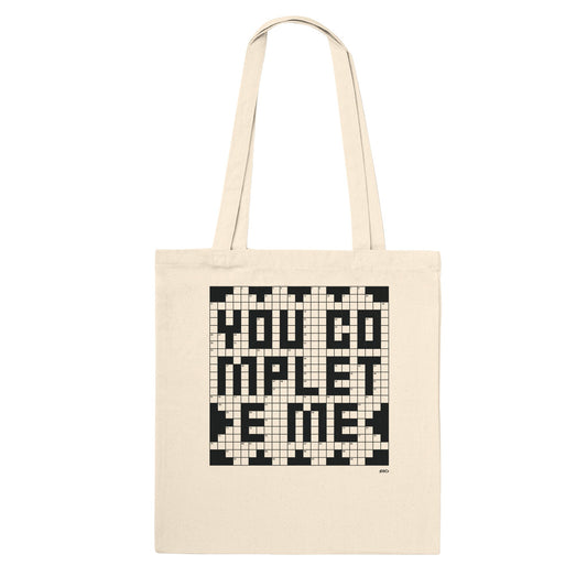 A white tote bag with a crossword puzzle graphic that reads You Complete Me